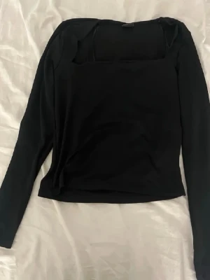 Svart långärmad topp från Gina - Svart långärmad topp från Gina  med fyrkantig ringning. Tunn och stretchig i materialet, perfekt att styla med jeans eller kjol. Enkel och stilren design som passar till många olika looks.
