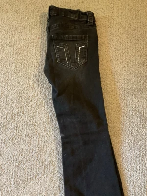 Svarta bootcut jeans - Snygga svarta jeans med bootcut-modell och coola nitar på bakfickan. Jeansen har klassisk femficksdesign, bälteshällor och knappgylf. Perfekta för dig som vill ha en edgy och trendig look.