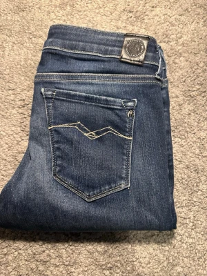 Mörkblå skinny jeans från Replay - Snygga mörkblå skinny jeans från Replay med klassisk femficksdesign och coola slitningar framtill. Jeansen har kontrastsömmar och en liten Replay-logga vid fickan. Perfekta för en trendig och avslappnad stil.