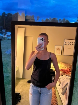 Svart linnetopp från Åhléns  - Säljer en enkel och stilren svart linnetopp från Åhléns Woman i storlek M. Toppen har tunna axelband och ärmlös design, perfekt för varma dagar eller som lager under en skjorta. Materialet känns mjukt och följsamt mot huden.