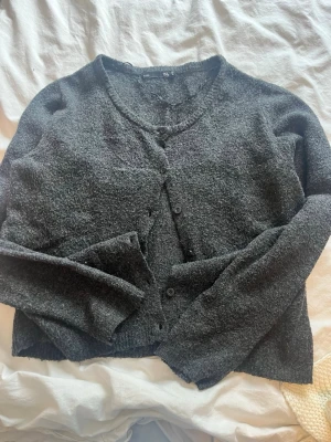 Mörkgrå kofta från 157. - Mysig mörkgrå kofta från 157. Koftan har rund halsringning, knäppning framtill med knappar och är tillverkad i ett mjukt, stickat material. Perfekt att slänga på sig när det är kyligt ute.