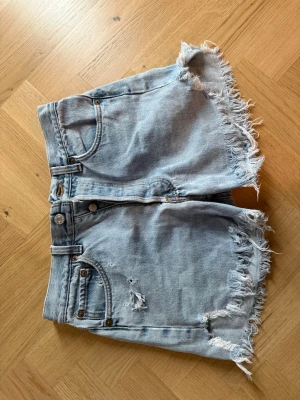 Ljusblå Levi's jeansshorts med fransar - Säljer ett par ljusblå jeansshorts från vintage Levi's med råa, fransiga kanter och klassisk femficksdesign. Shortsen har medelhög midja och slitna detaljer. Står inte storlek men passar mig som är 26/27. 