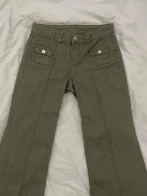 Olivgröna jeans med fickor - Säljer ett par olivgröna jeans med dekorativa fickor framtill. Jeansen är i storlek 36 och nästa aldrig använda. Säljer då dom är lite för korta på mig som är 178cm.