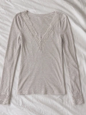 Beige intimissimi tröja  - Mjuk och bekväm beige långärmad topp med v-ringning och spetsdetaljer vid halsen och ärmsluten. Perfekt för avslappnade dagar hemma eller som ett mysigt lager under kalla kvällar.