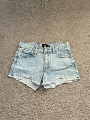 Ljusblå Jeansshorts  - Säljer ett par ljusblå jeansshorts med fransig kant och slitna detaljer framtill. Är i normal/lågmidjad form och har aldrig kommit till användning!