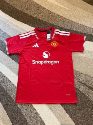 Manchester United 26-27 hemmatröja - Manchester United 26-27 hemmatröja  Storlek: M Namn och nummer: ingen Badge: ingen  Beskrivning: Tröjan är helt ny och felfri.  Säljs av ICEKIT icekit.se