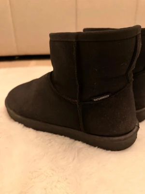 Svarta waterproof  boots - Säljer ett par svarta boots med låg skaft och mjukt, fluffigt foder på insidan. Skorna är tillverkade i ett vattenavvisande material och har en enkel, stilren design utan synliga loggor. Perfekta för kalla dagar när du vill hålla fötterna varma. Uggs liknande boots. En fläck från godis som går att ta bort. Förövrigt är de i nyskick