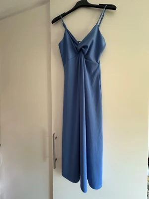 Blå långklänning  - En blå långklänning från H&M med smala axelband och v-ringad omlottdesign framtill. Klänningen har en lätt och pösigare passform. Använd ett fåtal gånger. 