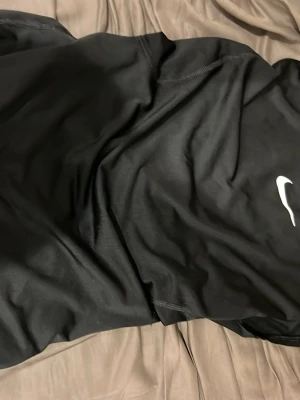 Svart Nike Pro linne - Säljer ett svart träningslinne från Nike Pro med klassisk vit Swoosh-logga på bröstet och 'NIKE PRO' tryckt i nacken. Linnet är ärmlöst och tillverkat i ett lätt, snabbtorkande material som passar perfekt för intensiva träningspass.