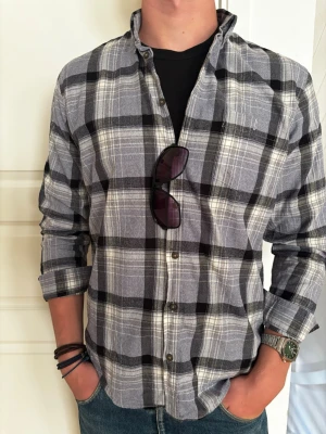 Flanell skjorta  - Säljer en rutig skjorta med knappar framtill. Skjortan har lång ärm och klassisk krage, perfekt att bära öppen över en t-shirt för en avslappnad look.