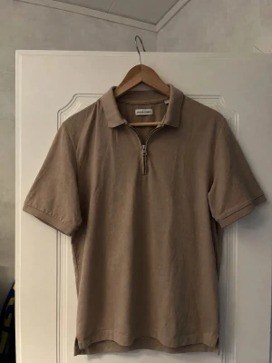 Beige half zip skjorta  - Snygg beige half zip tröja med korta ärmar och krage. Tröjan har en half zip-dragkedja framtill och är tillverkad i ett  bomullsliknande material. Enkel och stilren design som passar till många olika outfits.