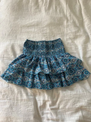 Blå mönstrad kortkjol Meet x Tiger - Kortkjol från Meet x Tiger i blått med ett detaljerat mönster och smockad midja.  Inbyggda shorts. Säljer då den inte kommer till användning!
