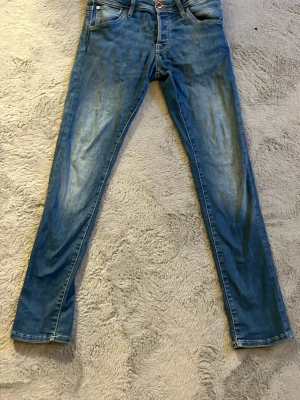 Blå skinny jeans med slitningar - Säljer ett par blå skinny jeans med lätt slitna detaljer och klassisk femficksmodell. Jeansen har normalhög midja och är tillverkade i denim med stretch för extra komfort. Perfekta till en avslappnad look.