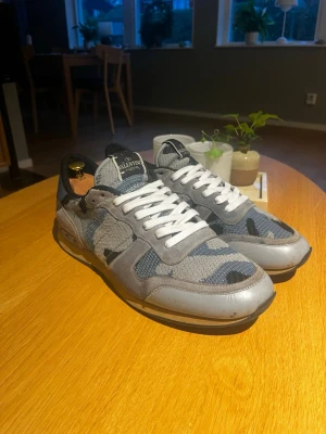 Valentino rockrunners - Ett par riktigt feta valentino rockrunners i en ljusblå färg med camo och med mocka och tyg material. Dom är lite använda och har nån pytte liten fläck som syns på en av bilderna samt lite lim rester typ på sulan som nog går bort om man försöker. Skorna är i en ovanlig färg som inte finns förfalskad och det är inga stora defekter. Dustbag följer med och för mer frågor kom PM.                   .               Nypris: 8000kr.       Strl:45