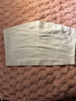 Vit bandeau tubtopp - Säljer en enkel och stilren vit bandeau tubtopp. Toppen är ärmlös och axelbandslös, perfekt för varma dagar eller som layering-piece. Tillverkad i mjukt bomullsmaterial för skön känsla och passform.