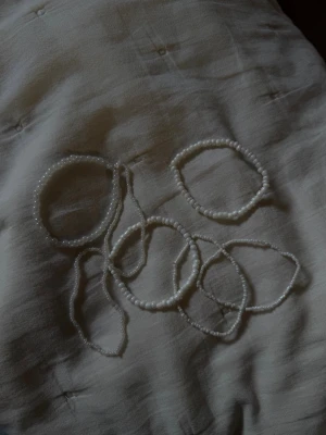 Vita pärlarmband i set - Säljer ett set med flera tunna armband gjorda av små vita pärlor. Armbanden har en enkel och stilren design och passar perfekt för att mixa och matcha med andra smycken. Alla armband är elastiska och lätta att ta på. 