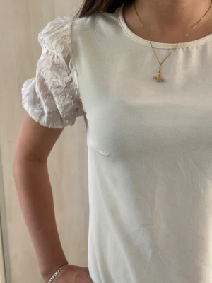 Vit topp med puffärmar och spetsdetaljer - Säljer en vit topp med genombrutna puffärmar i spets och blommönster. Toppen har rund halsringning och är i ett mjukt, lätt material. Perfekt för dig som gillar romantiska detaljer och vill ha en stilren look.