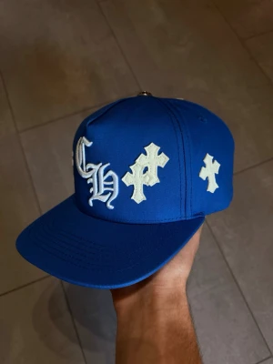 Blå keps med vita korsdetaljer - Keps från chrome hearts, kepsen är helt ny och i väldigt bra kvalité. Hör av dig vid fler frågor!