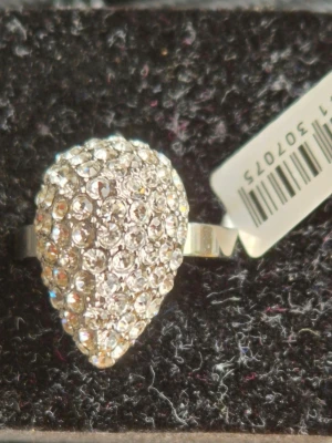 Silverfärgad ring med glittrande stenar från Edblad - Stilren ring i silverfärg med en stor droppformad topp täckt av gnistrande klara stenar. Ringen har en modern och iögonfallande design som verkligen drar blickarna till sig. Perfekt för dig som gillar att sticka ut med accessoarer.