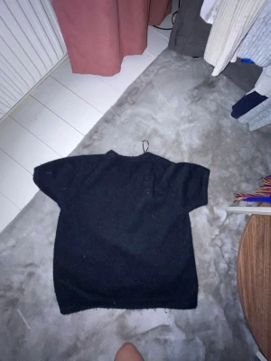 Svart stickad tröja Gina Tricot - En svart stickad tröja från Gina Tricot med korta ärmar och rund hals. Tröjan har en enkel och clean design som passar till det mesta. Perfekt för dig som gillar basic men ändå vill ha något mysigt och stilrent.