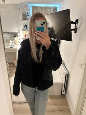 Svart croppad jacka med knappar - Säljer en svart croppad jacka med stora knappar framtill och bred krage. Jackan har lång ärm och en loose passform som ger en avslappnad look. Perfekt att slänga över en hoodie eller tröja för extra stilpoäng.