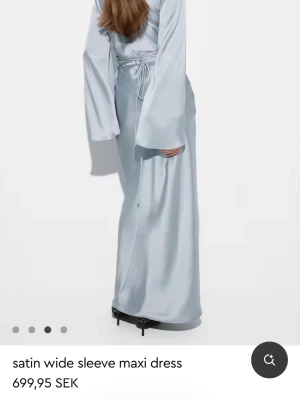 Ljusblå långklänning i satin - Snygg ljusblå långklänning i satin med vida ärmar och knytning i midjan. Klänningen har en elegant siluett och ett mjukt. Oanvänd, säljer den för 449kr. Ordinarie pris: 699.95kr