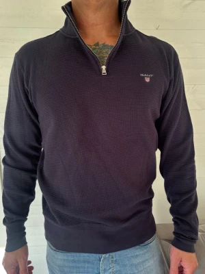Gant half zip - GANT half-zip tröja marinblå färg.  Snygg och stilren tröja från GANT med half-zip och hög krage. Våffelstruktur i tyget och GANT-logga på bröstet. Tröjan är i fint skick och passar perfekt till både jeans och chinos.  Hör gärna av dig vid intresse!