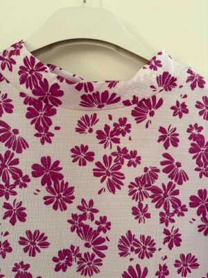 Vit blus med rosa blommor - Supersöt vit blus med rosa blommigt mönster och hög hals. Materialet är lätt och har en strukturerad yta som ger en skön känsla. Perfekt för dig som vill ha en färgglad och somrig look. Kolla gärna mina andra annonser❗️