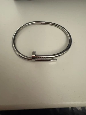 Silverfärgat armband i spikdesign - Snyggt armband i silverfärgad metall med unik spikformad design. Armbandet har en minimalistisk och modern look med rundad form och detaljer som liknar ett böjt spikhuvud. Perfekt för dig som gillar stilrena accessoarer med edge.