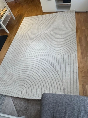 Beige matta med cirkelmönster - Säljer en stor, rektangulär matta i beige med upphöjt cirkelmönster. Mattan har en modern och stilren design som passar perfekt i vardagsrummet eller sovrummet. Materialet är  mjukt och mattan ger ett lugnt intryck till rummet.