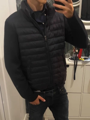 Mörkblå quiltad cardiganjacka  - Mörkblå cardiganjacka med quiltad kropp och släta ärmar. Jackan har dragkedja framtill, hög krage och elastisk nederkant. Perfekt för kyliga dagar på vintern, våren och hösten. Storlek 170 Köpt för 2200 på boozt.