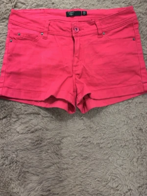 Rosa shorts med fickor och knapp - Snygga rosa shorts med klassisk femficksdesign och knappstängning fram. Shortsen har bälteshällor och är perfekta för varma dagar. Säljer eftersom den inte kommer till användning längre