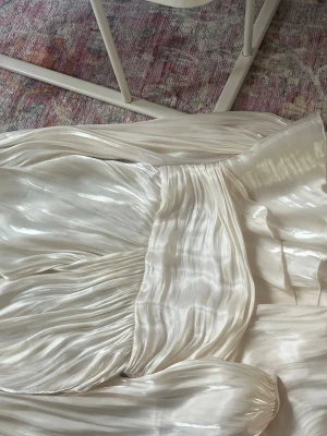 Vit långkjol i satin från Gina Tricot - Säljer en glansig vit långkjol från Gina Tricot i satinliknande material. Kjolen har ett plisserat fall och bred resår i midjan för en snygg siluett. Perfekt för dig som vill ha en elegant och flowy look.