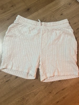 Vita strukturerade shorts med snörning - Säljer ett par vita shorts med snygg struktur och elastisk midja med snörning. Shortsen har en avslappnad passform och är perfekta för varma dagar. Tillverkade i ett lätt och bekvämt material som känns skönt mot huden.