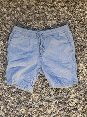 Ljusblå shorts med snörning - Säljer ett par ljusblå shorts i linne- och bomullsblandning. De har elastisk midja med snörning och två sidofickor. Perfekta för varma dagar och riktigt sköna att bära. Svarar snabbt vid frågor 