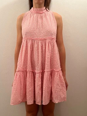 Rosa ärmlös volangklänning Lisa Marie Fernandez - Söt design  rosa klänning med volanger och strukturmönster. Ärmlös modell med knyt i nacken och lätt A-linjeformad passform. Perfekt för varma dagar och somriga tillfällen.