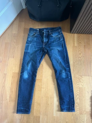 Levi's 512 Slim Taper W30 L30 – Mörkblå | Vintage wash - LEVI’S 512 SLIM TAPER  Storlek: W30 L30 Passform: Slim taper — sitter slim vid låret och smalnar av mot foten Färg: Mörkblå med naturlig vintage wash  512:an är Levi’s slim taper-modell — en modernare passform än 501:an med smalare ben som sitter snyggt utan att vara skinny. Mörkblå tvätt med subtil fading som funkar till det mesta.  Modellen på bilden är 175 cm och väger 65 kg — jeansen sitter tajt och modernt längs benet.  Skick: Mycket bra skick utan defekter. Nypris: ca 1 099 SEK