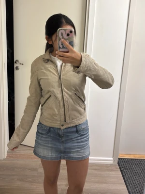 Beige skinnjacka med dragkedjor - Snygg beige skinnjacka med hög krage och dragkedja framtill. Jackan har två snedställda fickor med dragkedjor och markerad midja för en schysst passform. Perfekt till jeans eller kjol för en cool look. Väldigt många fläckar på jackan och ganska sliten av tidigare ägaren, säljer eftersom den är helt paj när jag köpte den och vill inte ha kvar den