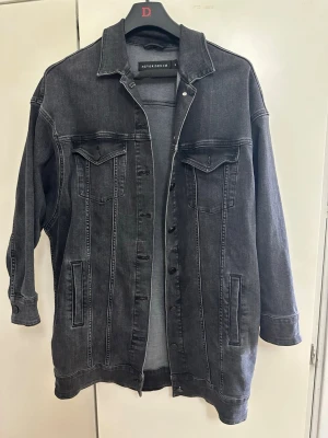 Svart jeansjacka från Never Denim - Snygg svart jeansjacka från Never Denim i storlek S. Klassisk modell med två bröstfickor med lock och knappar, samt två sidofickor. Jackan har en rak passform och silverfärgade knappar framtill. Perfekt för dig som gillar en stilren och avslappnad look.
