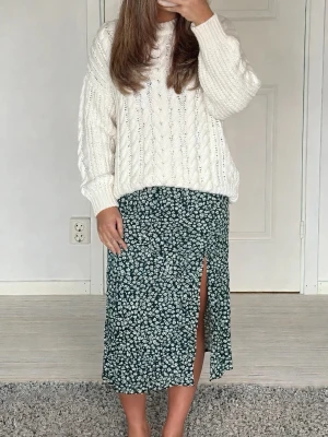 Grön blommig kjol med slits - Supersnygg grön kjol med vitt blommönster och en trendig slits framtill. Kjolen har en rak passform och är perfekt för dig som gillar en avslappnad men ändå stilren look. Längden är mitt på vaden och materialet känns lätt och skönt.
