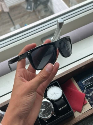 Svarta Ray-Ban solglasögon Wayfarer - Säljer ett par klassiska svarta Ray-Ban Wayfarer solglasögon med mörka glas. Snygg och tidlös design med Ray-Ban-logga på sidan. Perfekta för att höja din stil i solen.