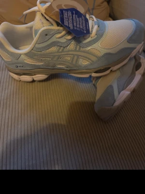 Vita och ljusblå Asics sneakers -  Snygga sneakers från Asics i ljusblått, storlek 43 självklart ingår box. inte används i överhuvudtaget pågrund av att dom satt dåligt på mig och gick ej att skicka tillbaka drf säljs dom nu!