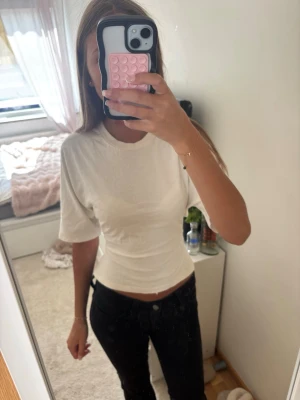 Vit topp med knyt och öppen rygg - Snygg vit topp i bomull med korta ärmar och tight passform. Toppen har öppen rygg med knytband som ger en unik och trendig look. Perfekt till jeans eller kjol för en cool stil.