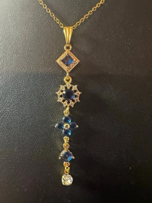 Guldhalsband med blå stenar - Unikt halsband i guldton med flera blå stenar i olika former och en klar sten längst ner. Hänget har geometriska och blommiga detaljer som ger ett elegant och trendigt intryck. Perfekt för dig som vill sticka ut med accessoarer.