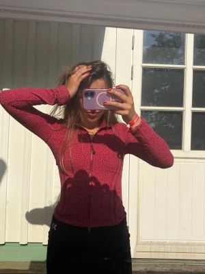 Mörkröd ziptröja med mönster - Säljer en mörkröd ziptröja med diskret mönster och lång ärm from. Tröjan har dragkedja framtill och en figurnära passform. Perfekt för dig som gillar sportig och avslappnad stil.