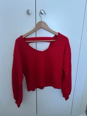 Röd stickad tröja från Bershka - Trendig röd stickad tröja från Bershka med bred, djup urringning och en dekorativ rem i ryggen. Långärmad modell med avslappnad passform och ribbade muddar. Perfekt för att lyfta din outfit med en färgklick.