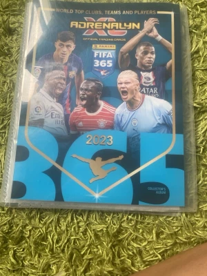Panini FIFA 365 Adrenalyn XL 2023 album - Säljer ett Panini FIFA 365 Adrenalyn XL 2023 samlaralbum med officiella fotbollssamlarbilder. Albumet innehåller flera Limited Edition- och Trophy Triumph-kort med spelare från olika toppklubbar. Perfekt för dig som gillar fotboll och samlarkort.