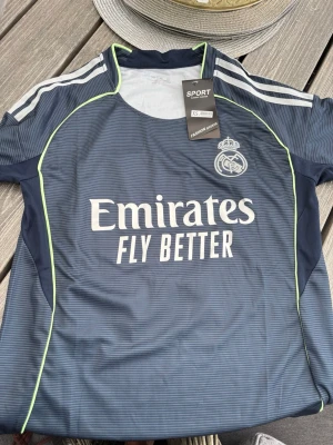 Real Madrid Mbappé matchtröja XS - Säljer en mörkblå Real Madrid matchtröja med Mbappé och nummer 10 på ryggen. Tröjan har vita detaljer, tunna ränder och neongula sömmar. Perfekt för fotbollsträning eller att bära som supporter. Materialet är lätt och andas bra.