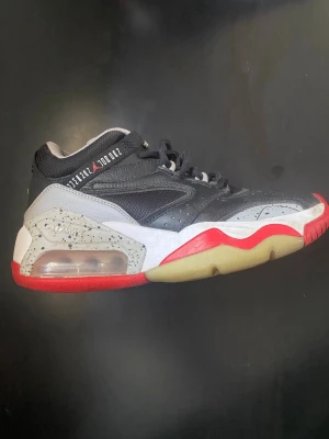 Svarta och grå sneakers med röd sula - Snygga sneakers i svart och grått med detaljer i vitt och rött. Skorna har en synlig luftbubbla i sulan, meshpaneler på sidan och en robust, sportig design. Yttersulan är delvis genomskinlig med röda och beige partier. Perfekta för dig som gillar streetwear.