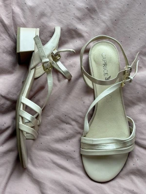 Klackar/sandaletter från Caprice.  - Klackar/sandaletter från Caprice i storlek 40         (6 1/2). De är använda ett fåtal gånger och är i fint skick. De är ljusrosa/cremefärgade, med detaljer i rose gold och beige/vit (remmarna). Undersulorna är bruna och spännena är guldfärgade. Klacken är ca 3,5 cm hög. Finns vissa tecken på användning, som t.ex. lite slitage på undersulorna och vissa väldigt små fläckar. 